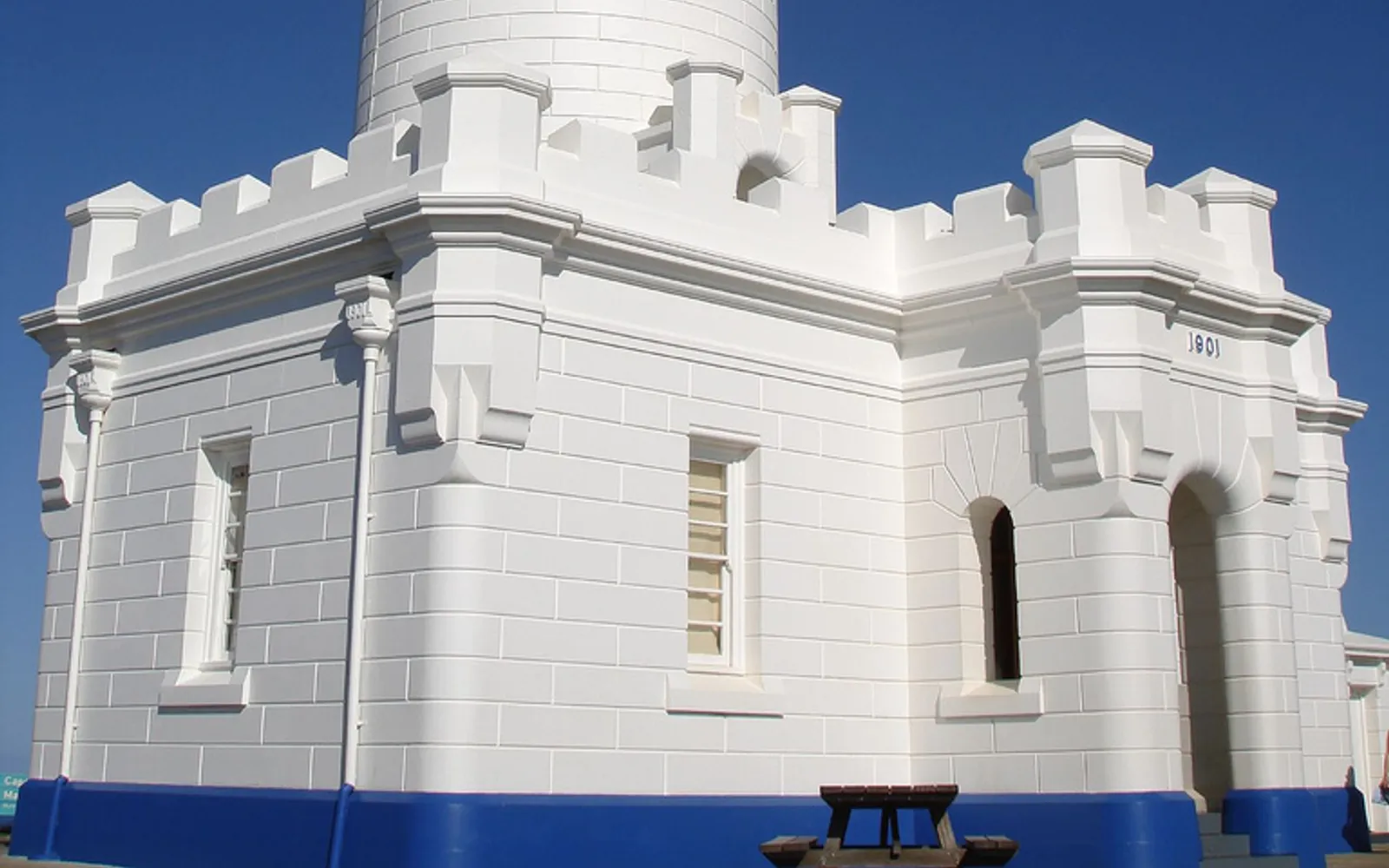 The white Cape Byron Lighthouse standing on a high cliff above deep blue sea, overlooking the whole bay and a wide-open horizon