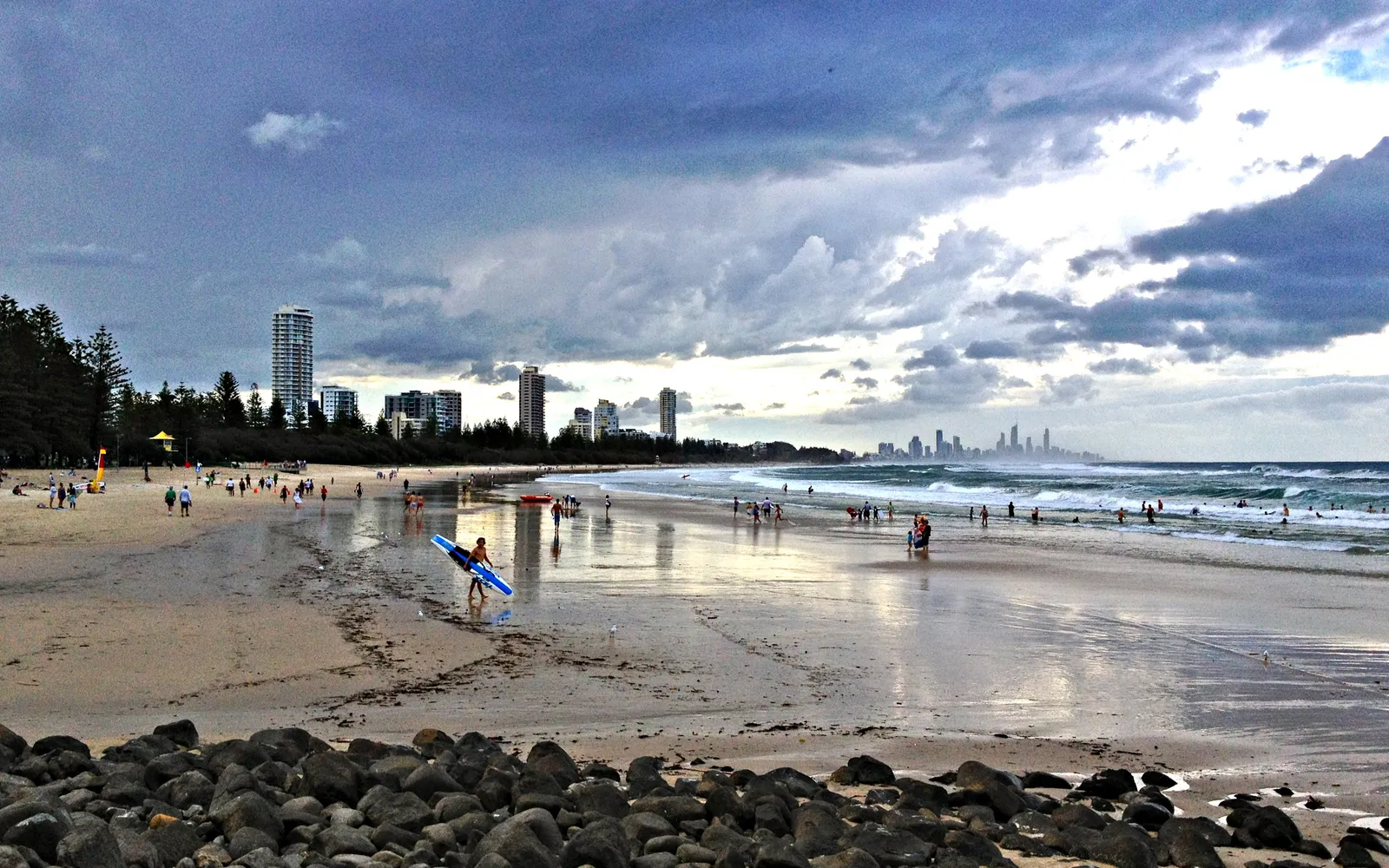 Aerial view over Burleigh Heads beach, a graceful curve of sand between dark grey rocks and lush green coastal forest