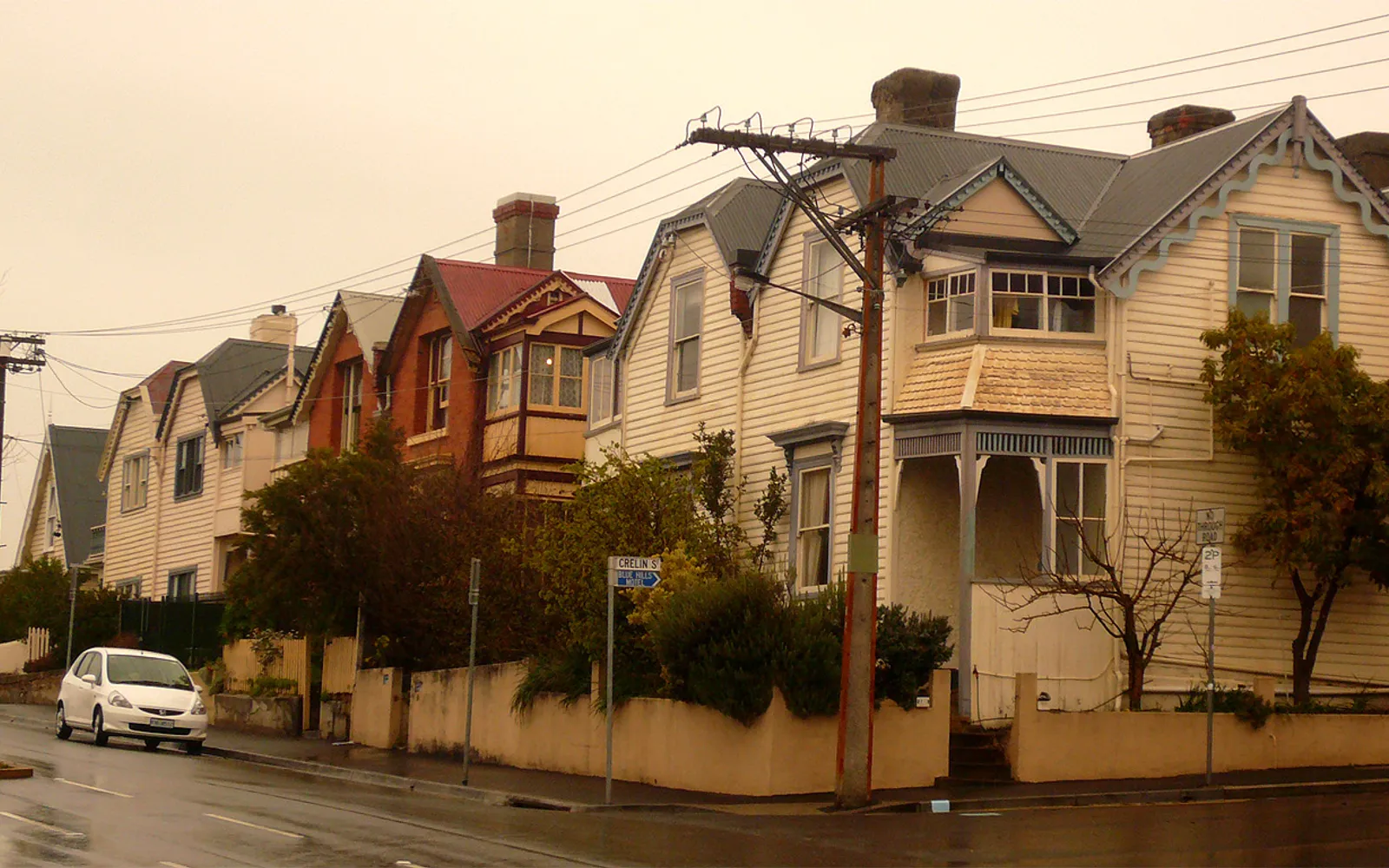 A narrow street in Battery Point, Hobart, lined on both sides with cream-coloured colonial sandstone houses and pretty ornamental flower gardens out front.