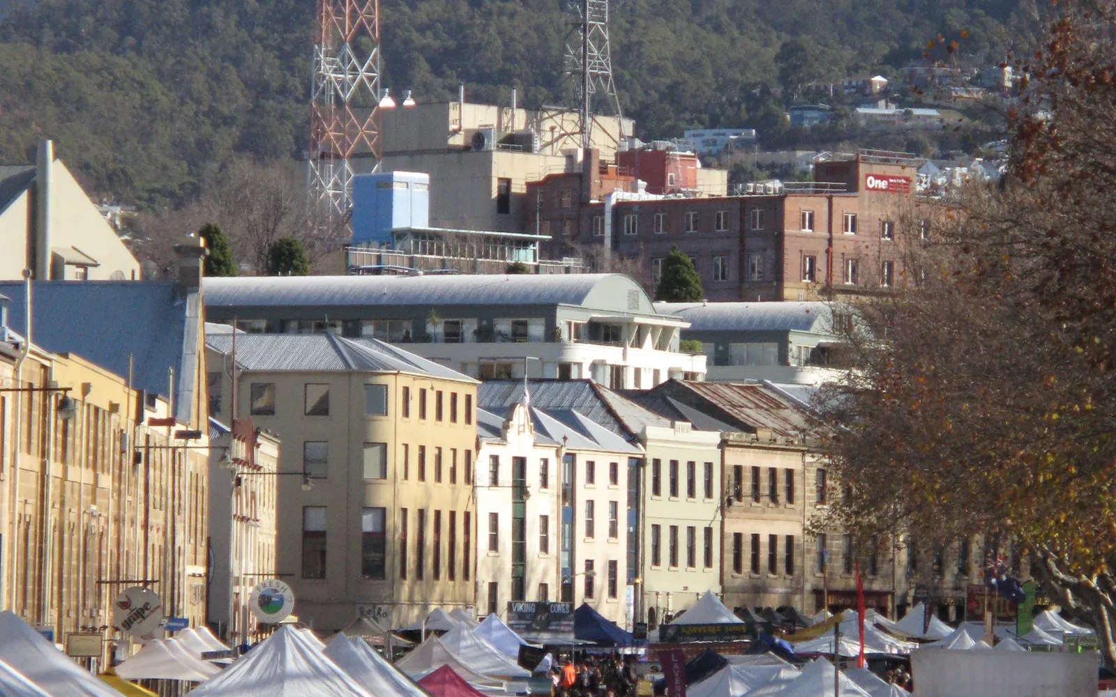 A row of honey-coloured colonial sandstone buildings at Salamanca Place, Hobart, with a busy morning market out front and stalls selling local produce and crafts lining the way.