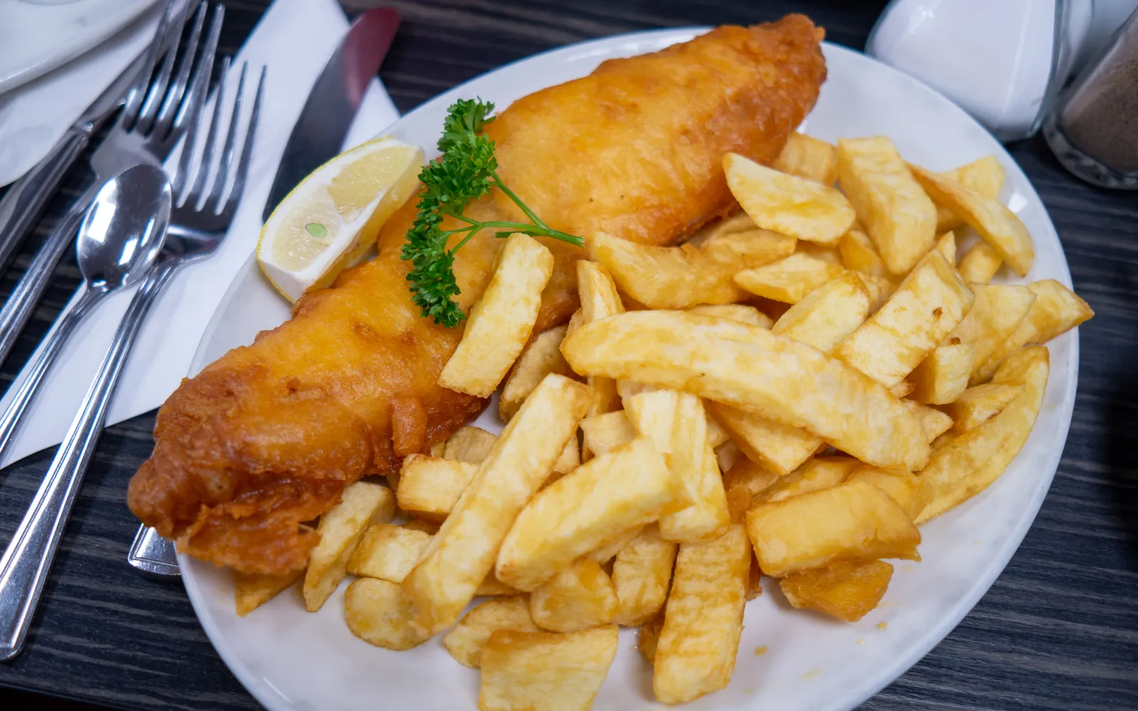 A tray of Australian-style fish and chips: a large piece of fish in golden, crisp batter served with lemon, tartare sauce and thick-cut chips.