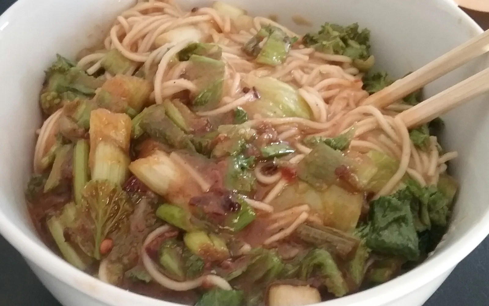 A bowl of suanlafen glass sweet-potato noodles in orange-red hot-and-sour broth with crunchy peanuts