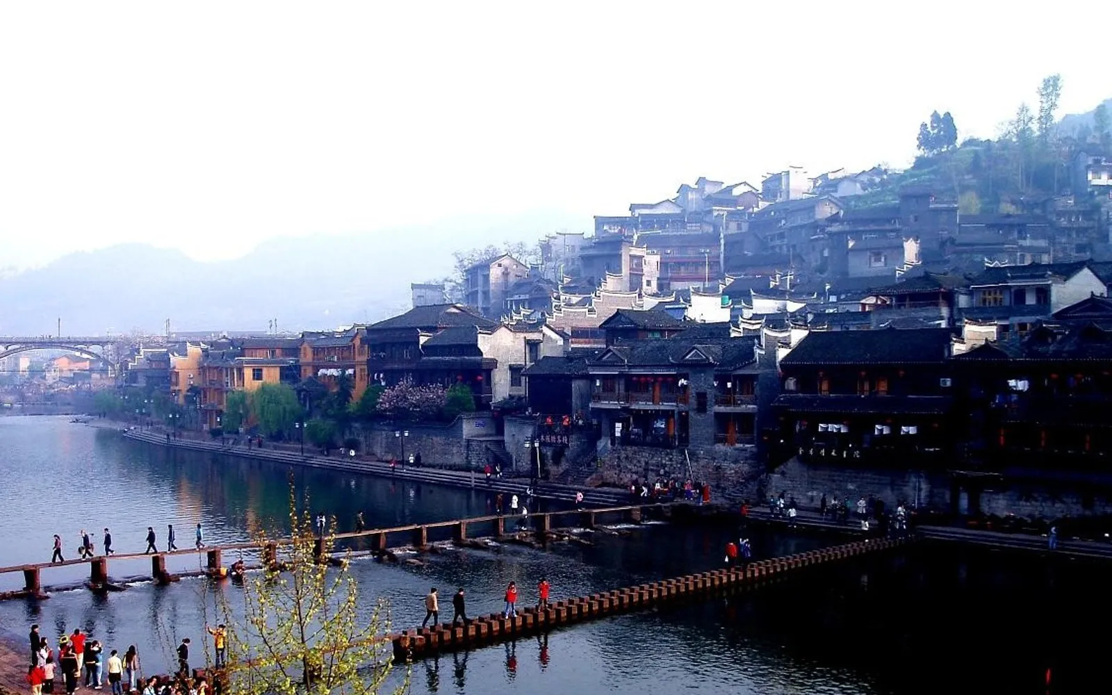 A wooden boat on the Tuojiang River passing in front of the Diaojiaolou stilted houses reflecting the evening lights