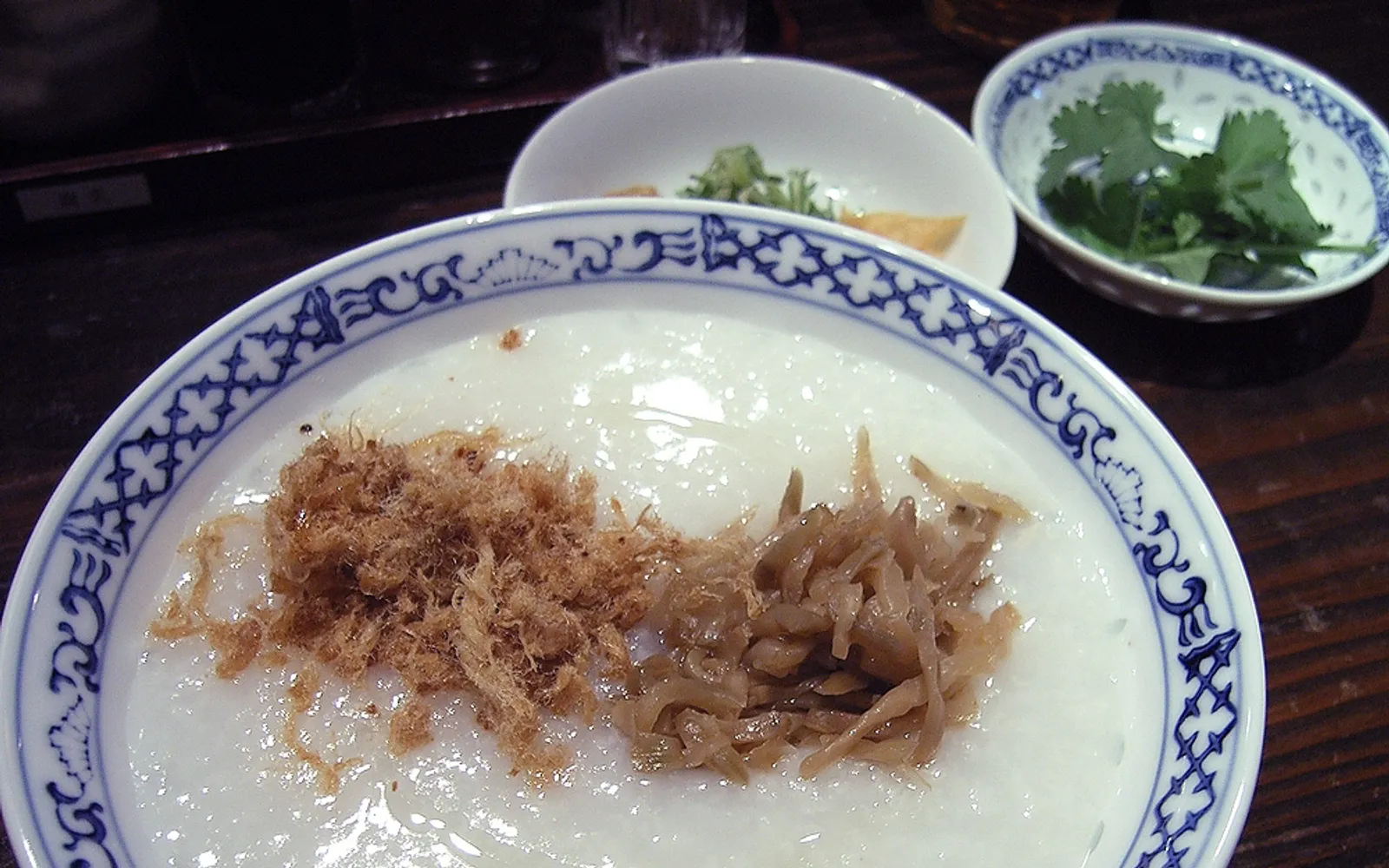 A bowl of creamy white Cantonese congee topped with fresh fish and chopped ginger, served in a Guangzhou ceramic bowl