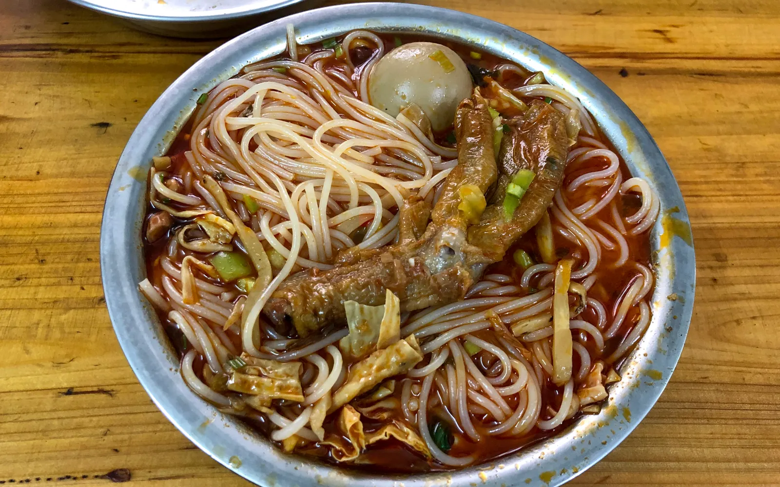 Guilin-style snail noodles, a deep bowl of rice noodles in thick orange snail broth topped with pickled mustard greens, long beans, fried tofu and red chili