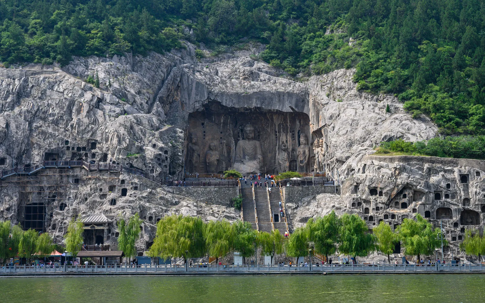 A colossal stone-carved Buddha at the Longmen Grottoes, the central Vairocana Buddha standing 17 metres tall, surrounded by bodhisattvas and a cliff face carved with exquisite craftsmanship