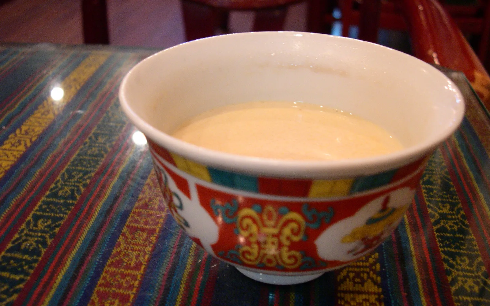 Warm brown yak butter tea in a traditional metal cup, set on a wooden table in a Tibetan tea house