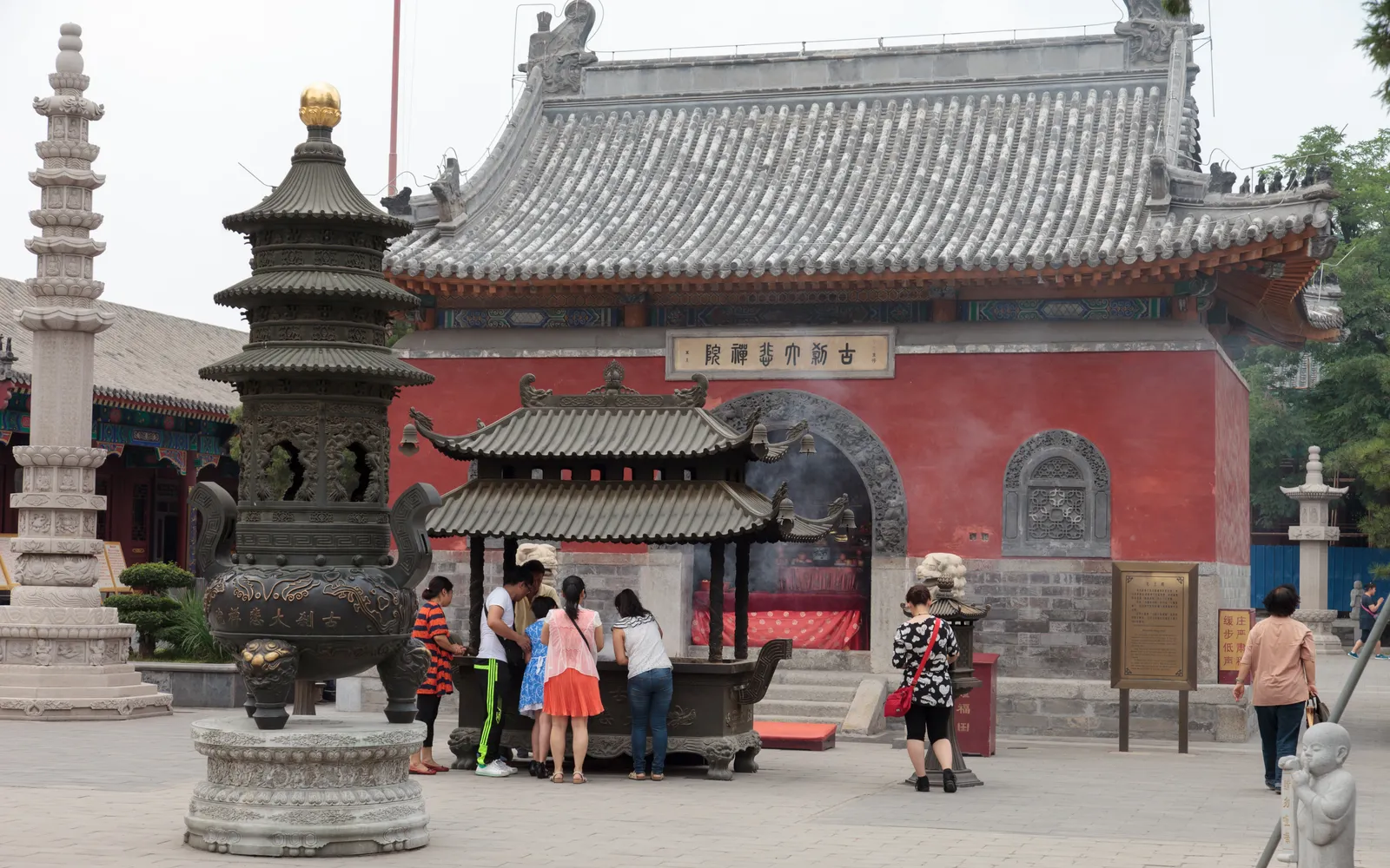 Inside Dabei Monastery Tianjin: a red-and-gold pagoda stands in a wide courtyard as worshippers light incense before a large Buddha statue