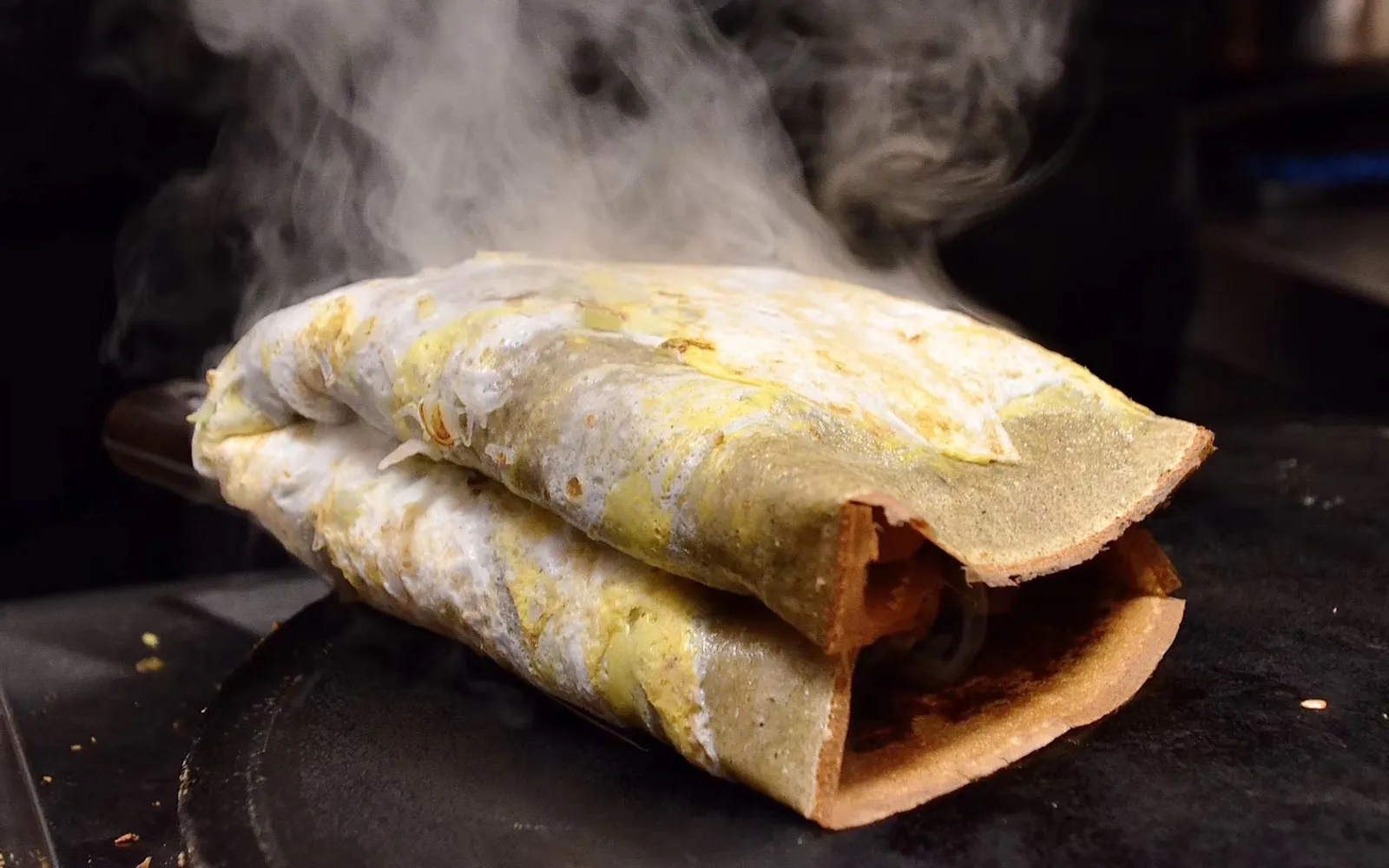 Jianbing being rolled on a round griddle — a thin egg spread over a mung-bean crepe, topped with a crispy fried cracker sheet and sweet soy paste, being wrapped for a customer