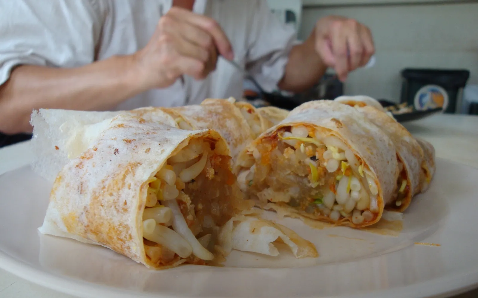 Xiamen popiah rolls on a plate — thin soft wrappers filled with braised turnip and vegetables, topped with sweet-salty dipping sauce, ground peanuts, dried shrimp, and fried egg