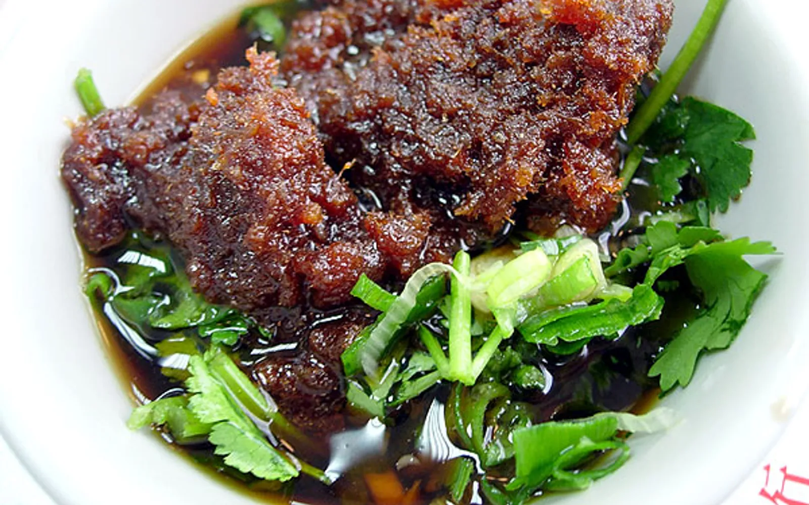 A bowl of Xiamen sa cha noodles — golden-brown broth fragrant with dried shrimp and coconut, yellow noodles, minced pork, spinach, and roasted peanuts