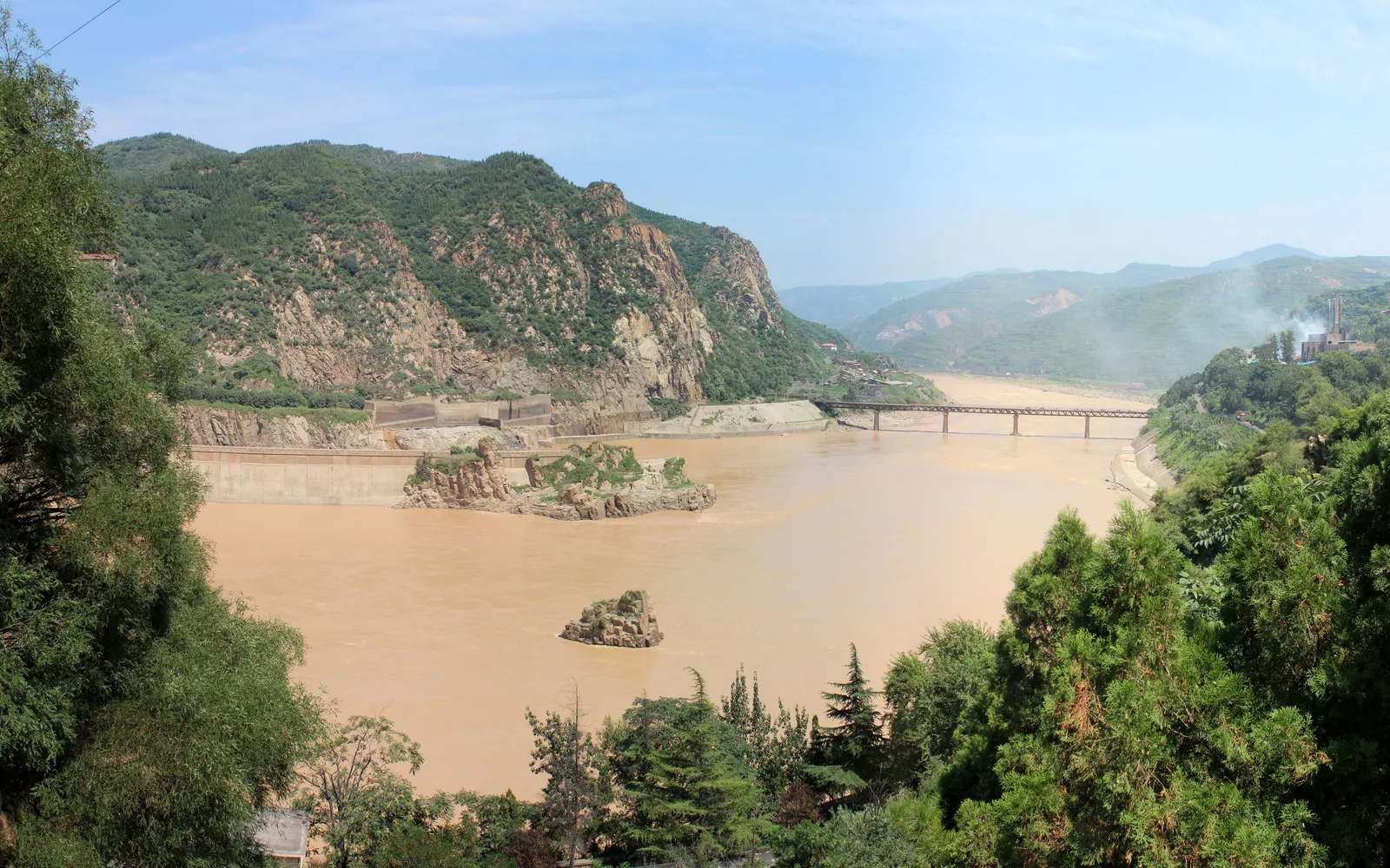 The Yellow River stretching to the horizon in rainy-season flood — golden-yellow water surging across the Henan plain in the late afternoon light