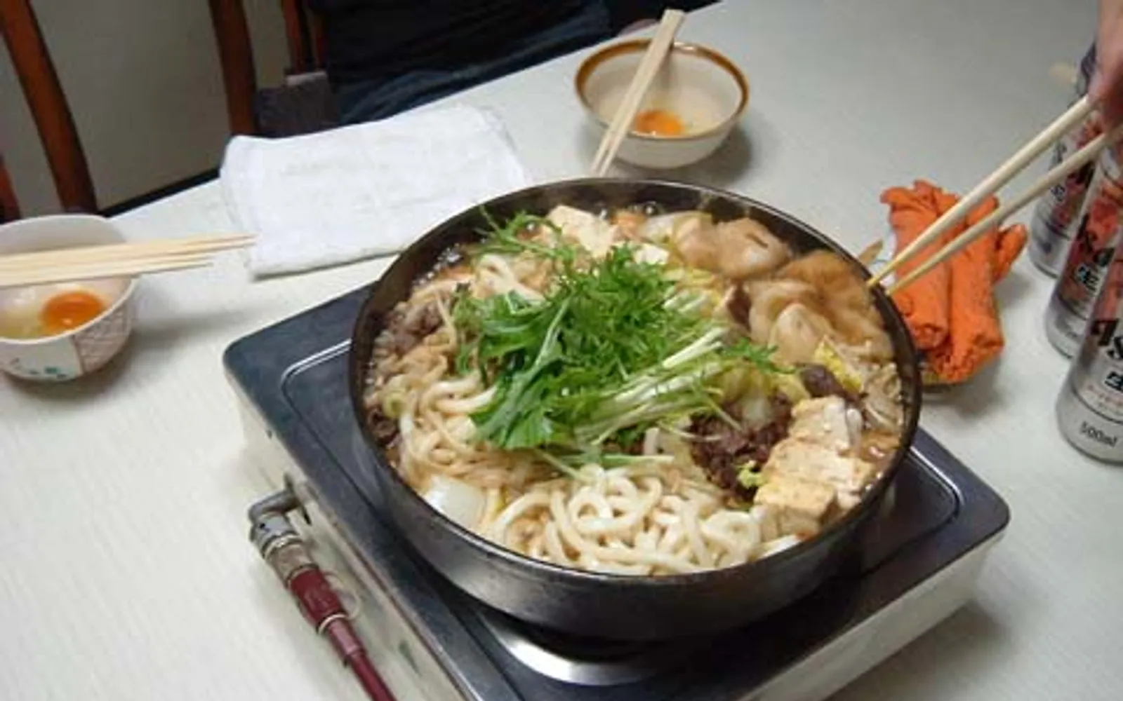 A pot of mizutaki with clear broth, chicken, and fresh vegetables cooking over a charcoal burner at the table