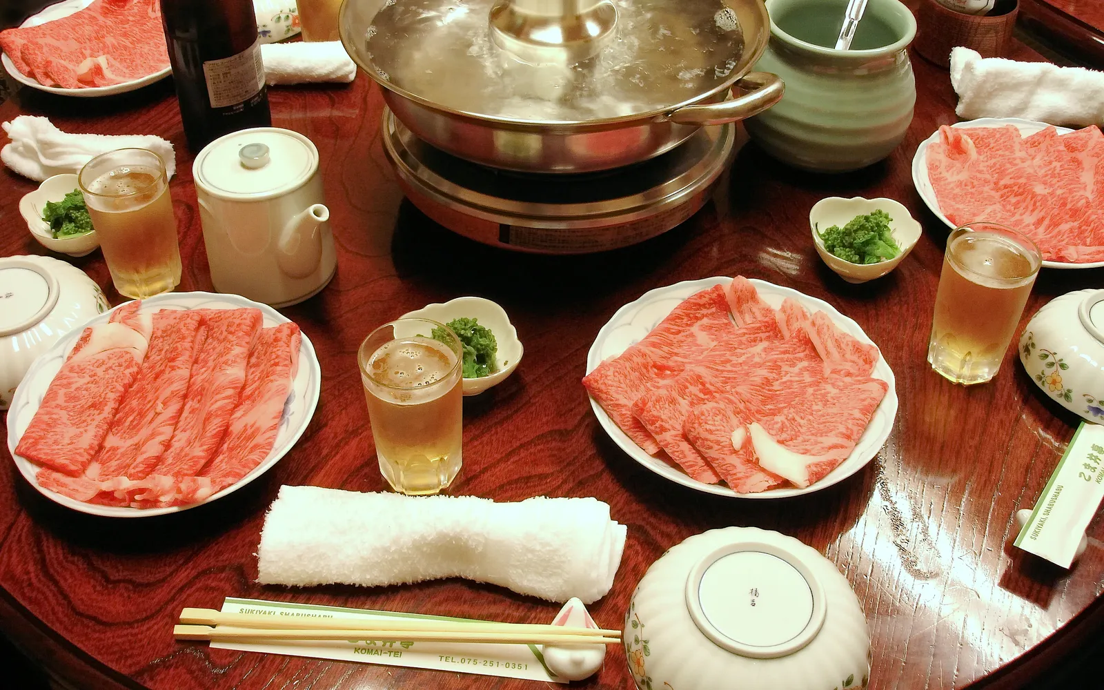 Thinly sliced pink Kurobuta pork fanned out beside a bubbling broth pot with fresh vegetables