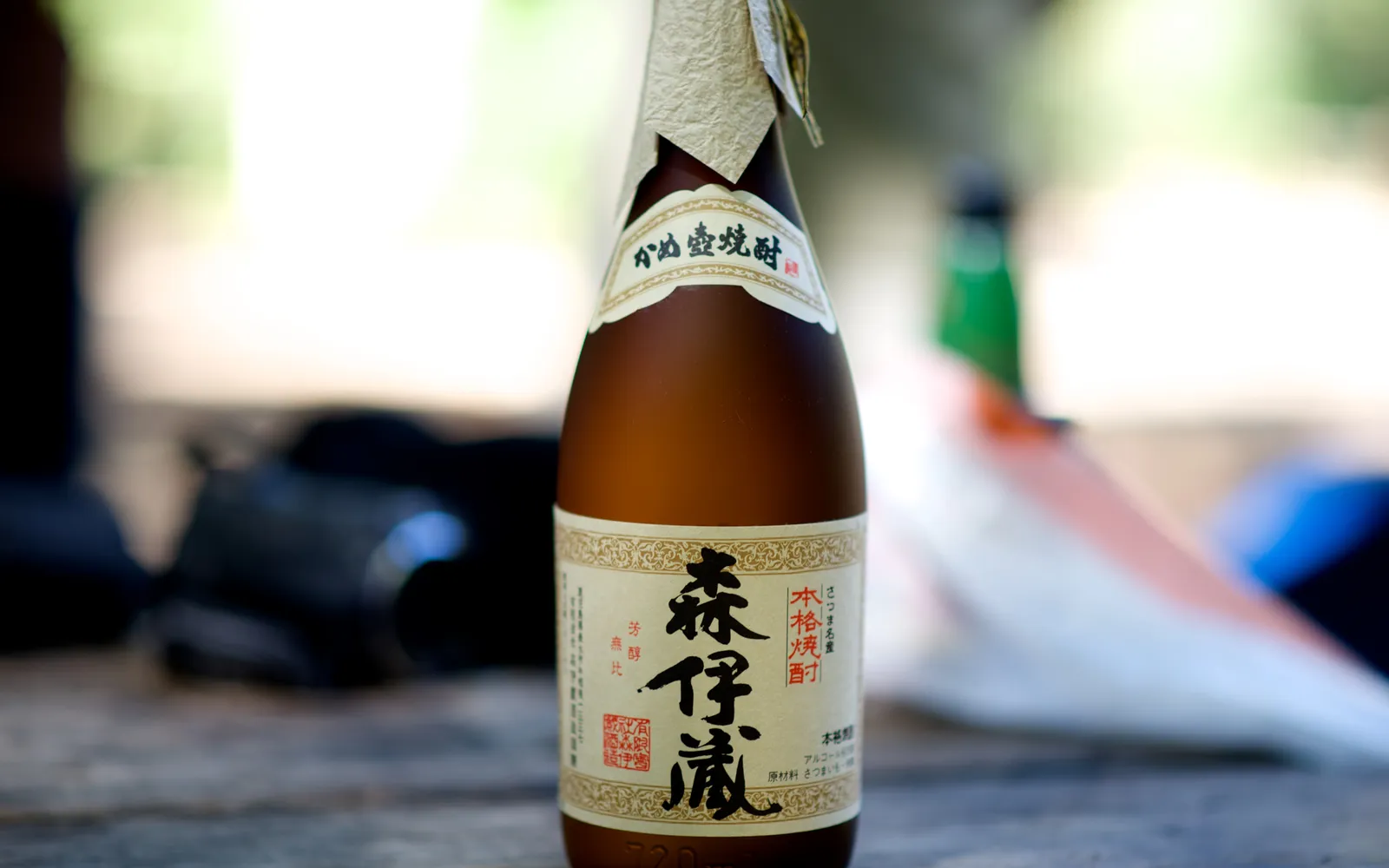 Premium Satsuma Shochu bottle on a wooden table with a glass of ice and purple sweet potato