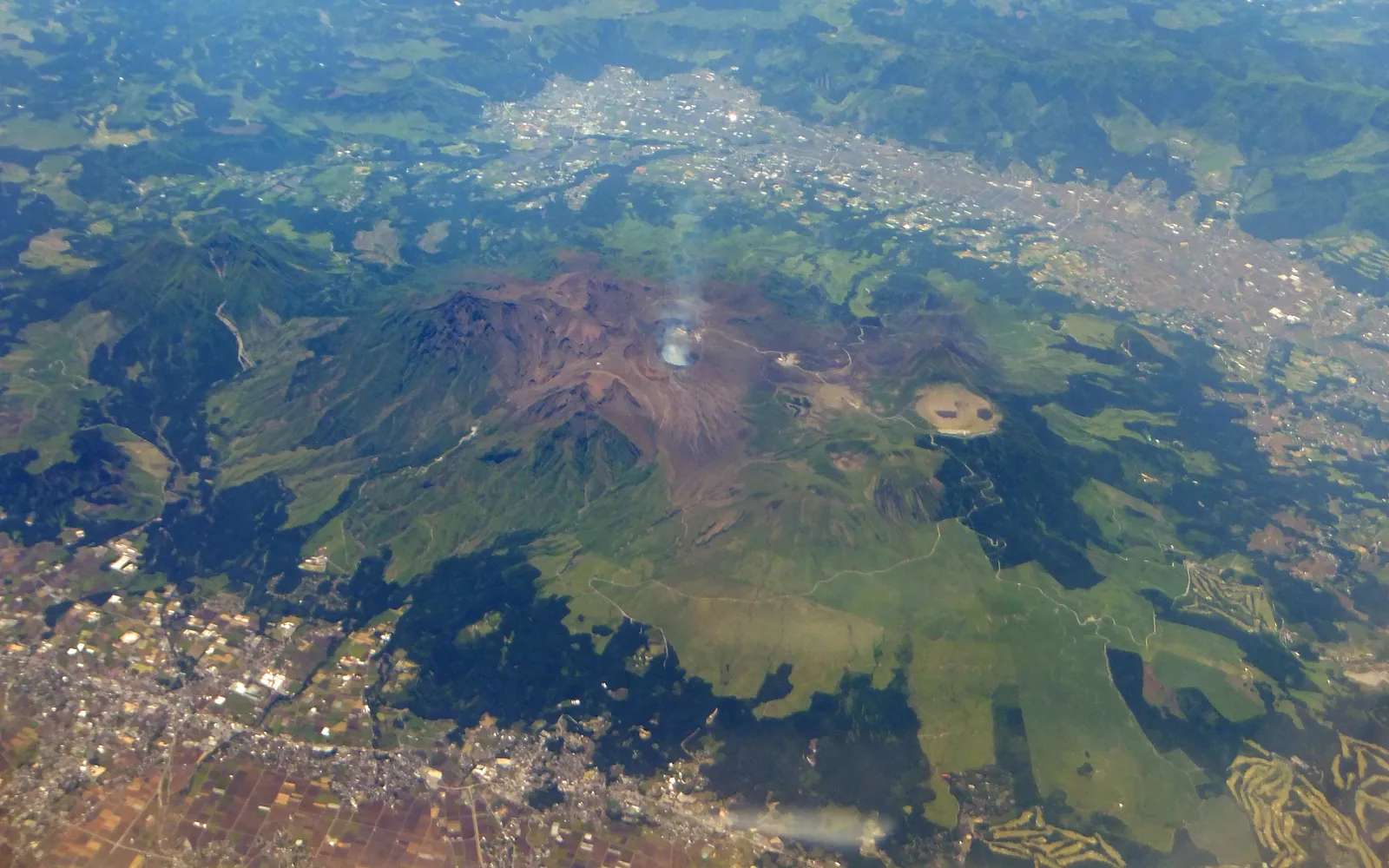 The blue-green crater lake of Nakadake with plumes of steam rising