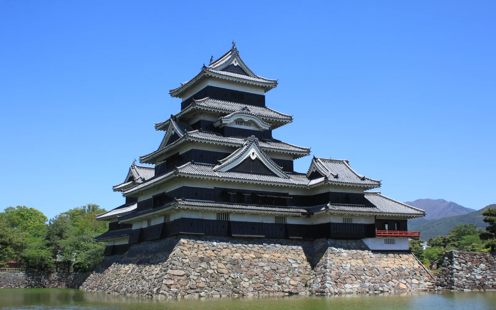 Matsumoto Castle's black walls reflected in the moat with cherry blossoms in full bloom
