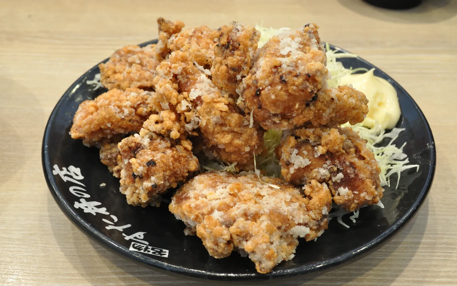 A large golden-crispy piece of sanzokuyaki fried chicken served on a plate with lemon and shredded cabbage