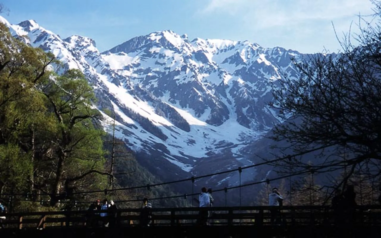 The blue Kappa-bashi bridge spanning the Azusa River with the Alps and green forest behind it