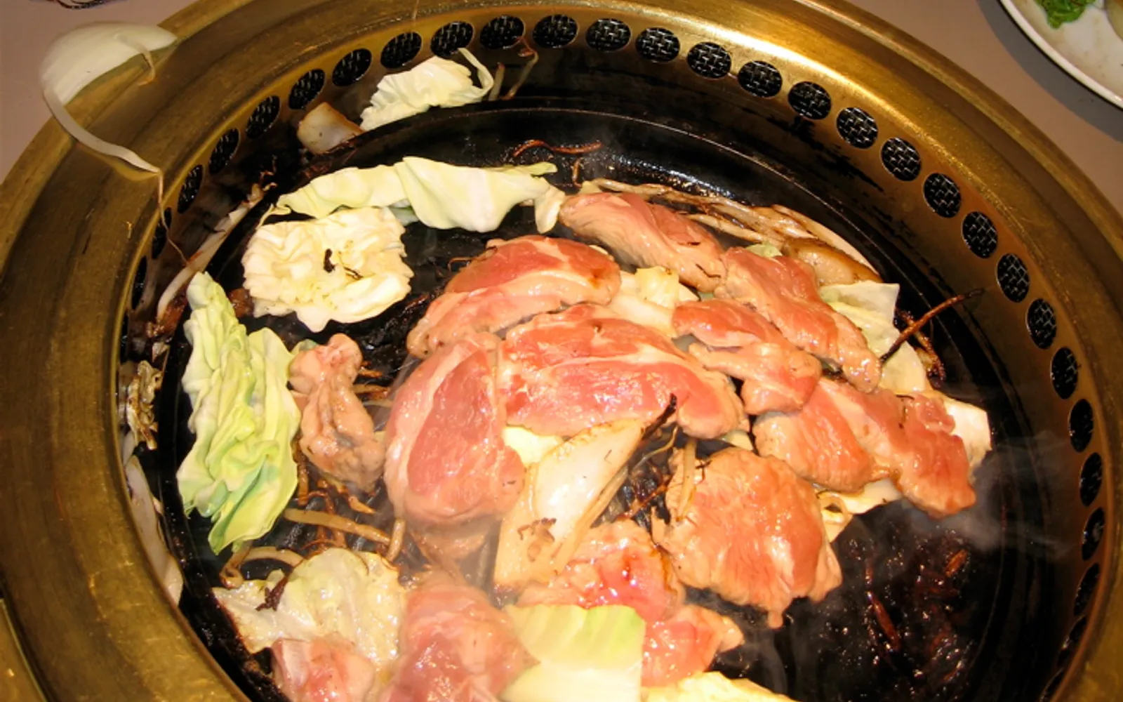 Lamb and vegetables sizzling on the domed cast-iron Jingisukan grill, smoke rising in a warm-lit restaurant