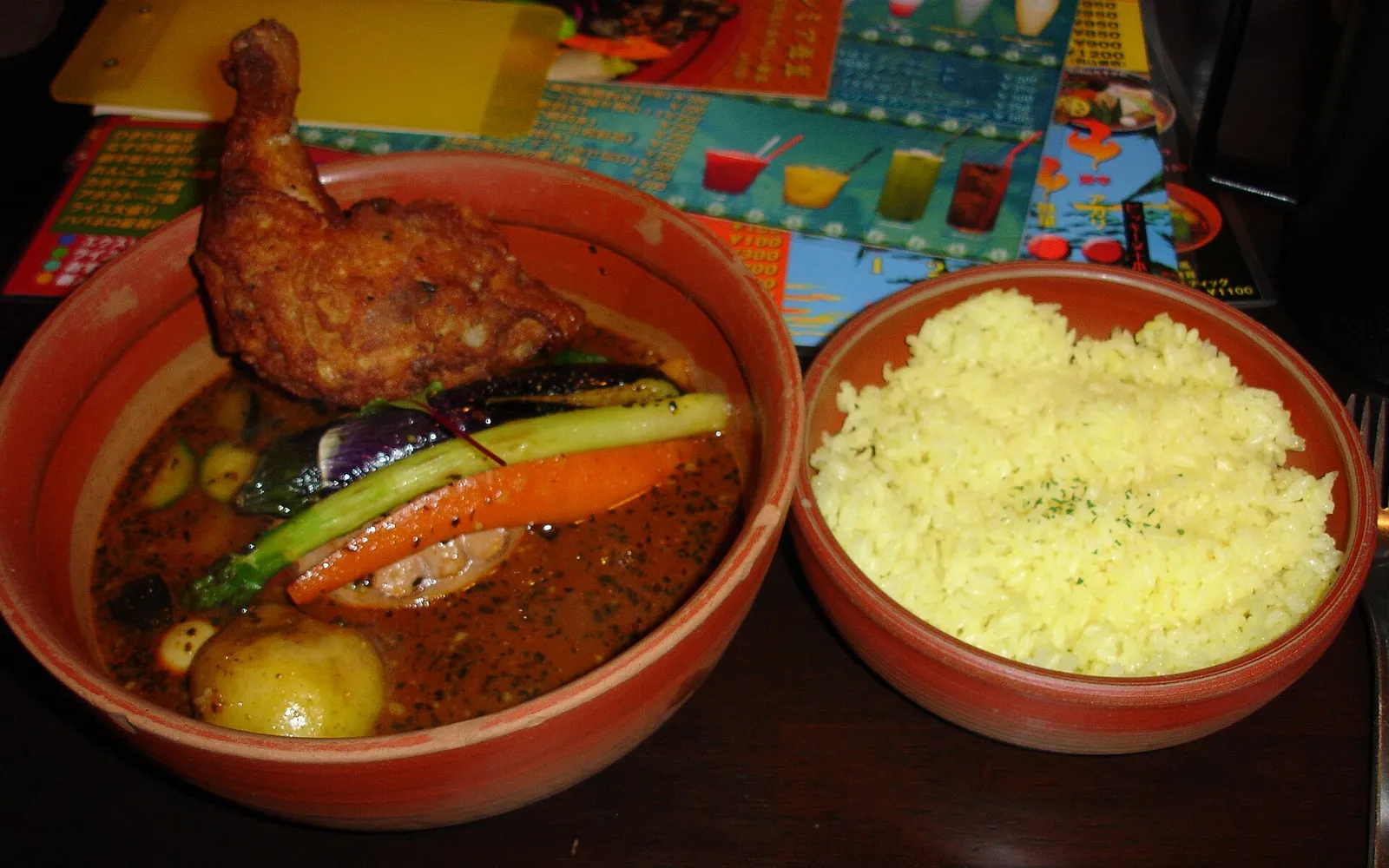 A deep-brown bowl of Sapporo soup curry packed with su-age fried vegetables, rice served in a separate bowl alongside