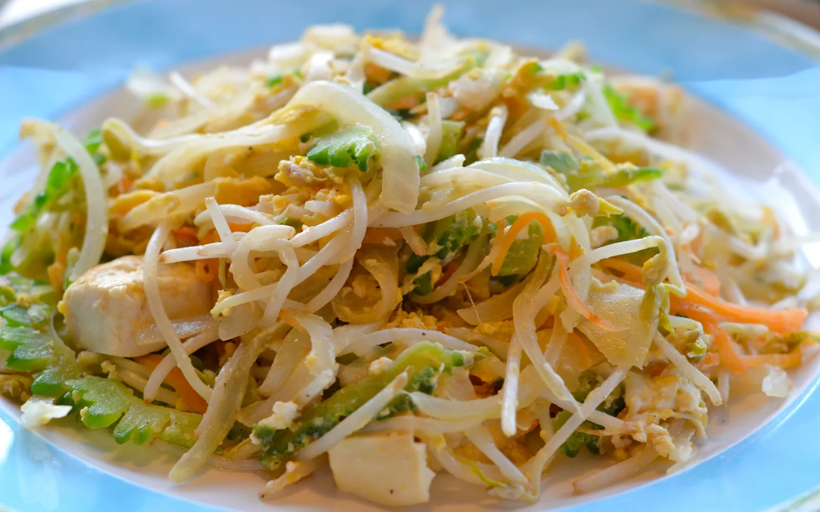Goya chanpuru with dark green bitter melon, egg, firm tofu, and pork in a hot iron pan — Okinawa's best-known everyday dish