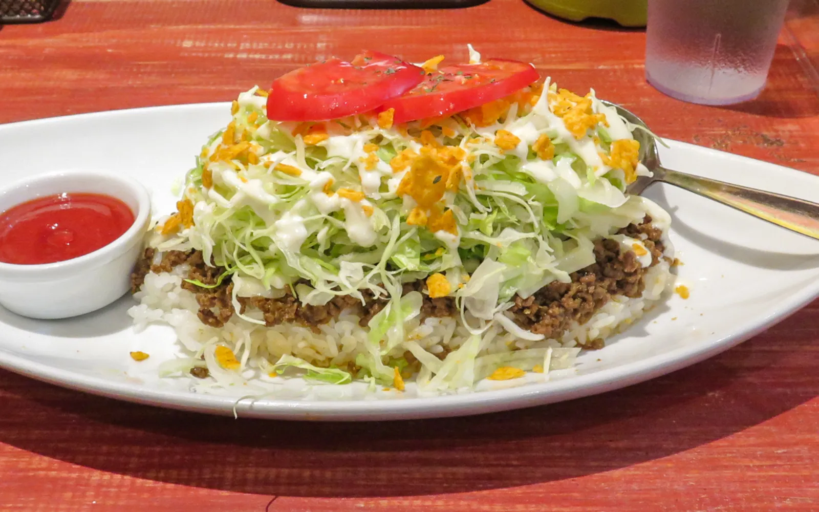 A large plate of taco rice — steamed white rice topped with spiced ground beef, cheese, shredded lettuce, tomato, and salsa