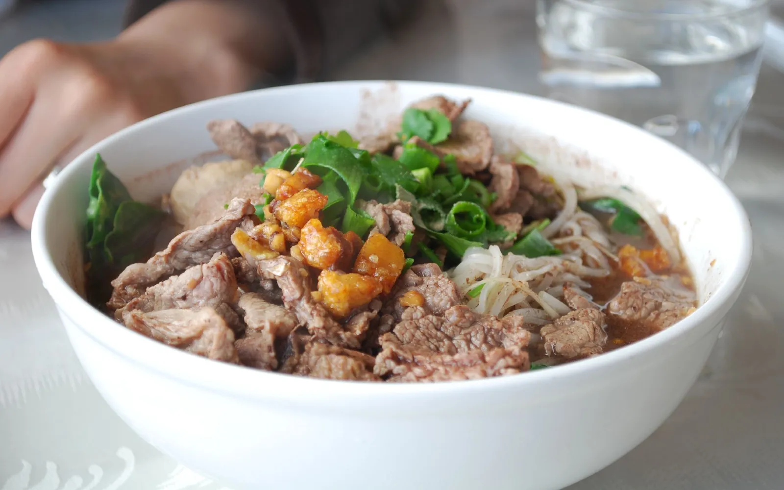 A small bowl of dark, intensely flavored boat noodles topped with pork and coagulated blood