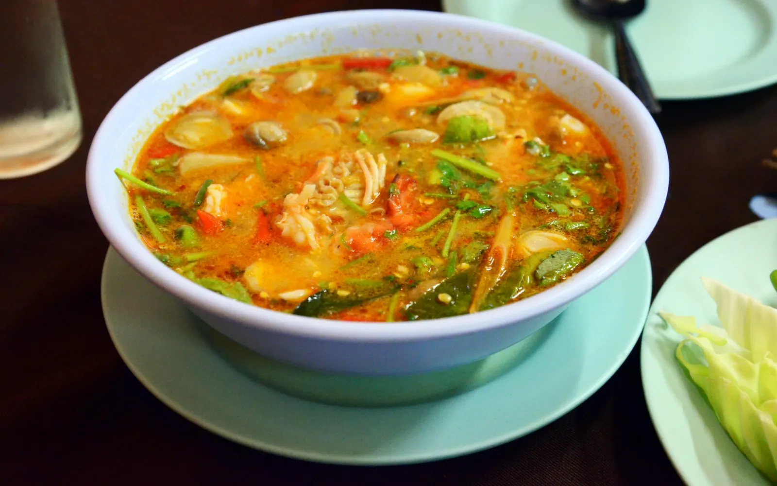 Tom Yum Goong in a hot clay pot — fresh river prawns, straw mushrooms, lemongrass, kaffir lime leaves floating in a rich orange-brown broth