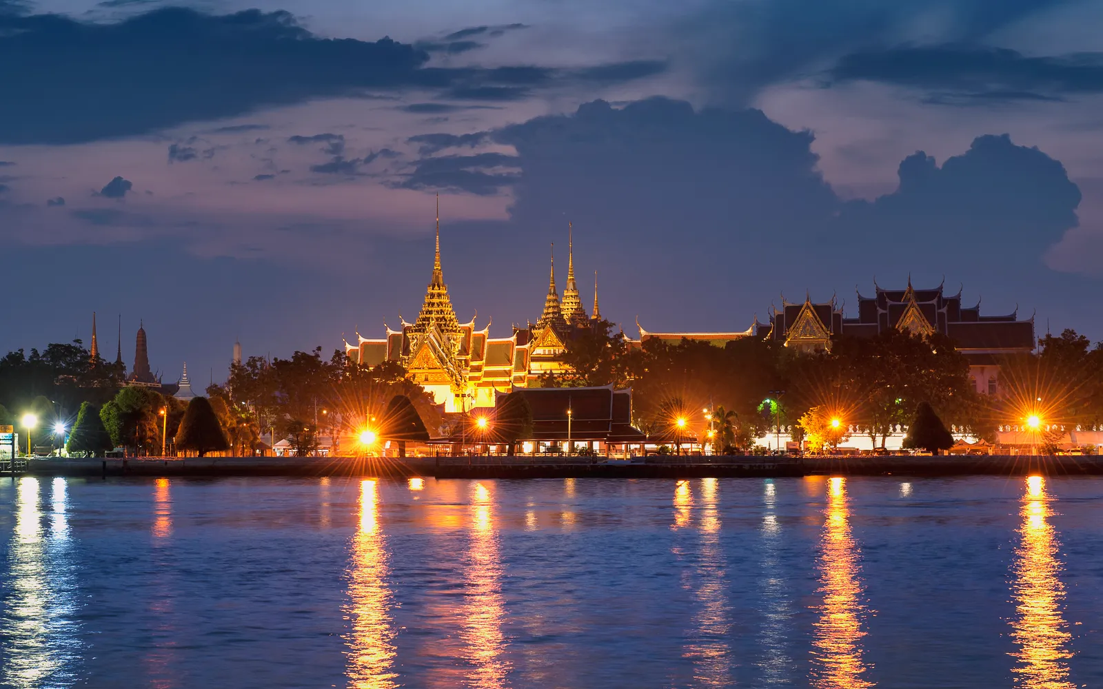 The Grand Palace and golden spires of Wat Phra Kaew in Bangkok against a bright blue sky