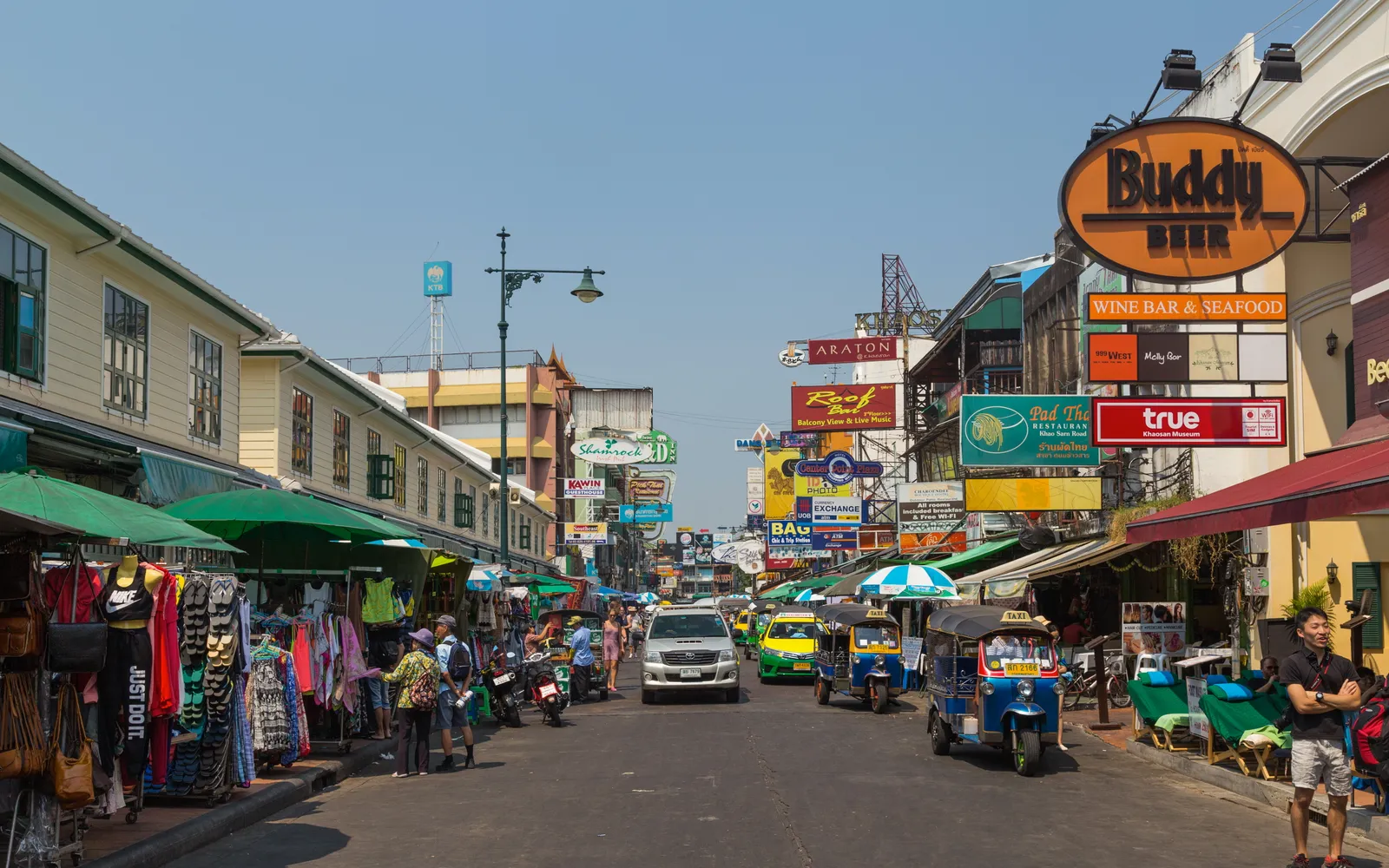 Khaosan Road in Bangkok at night, neon signs and shops lining both sides of the street, packed with visitors