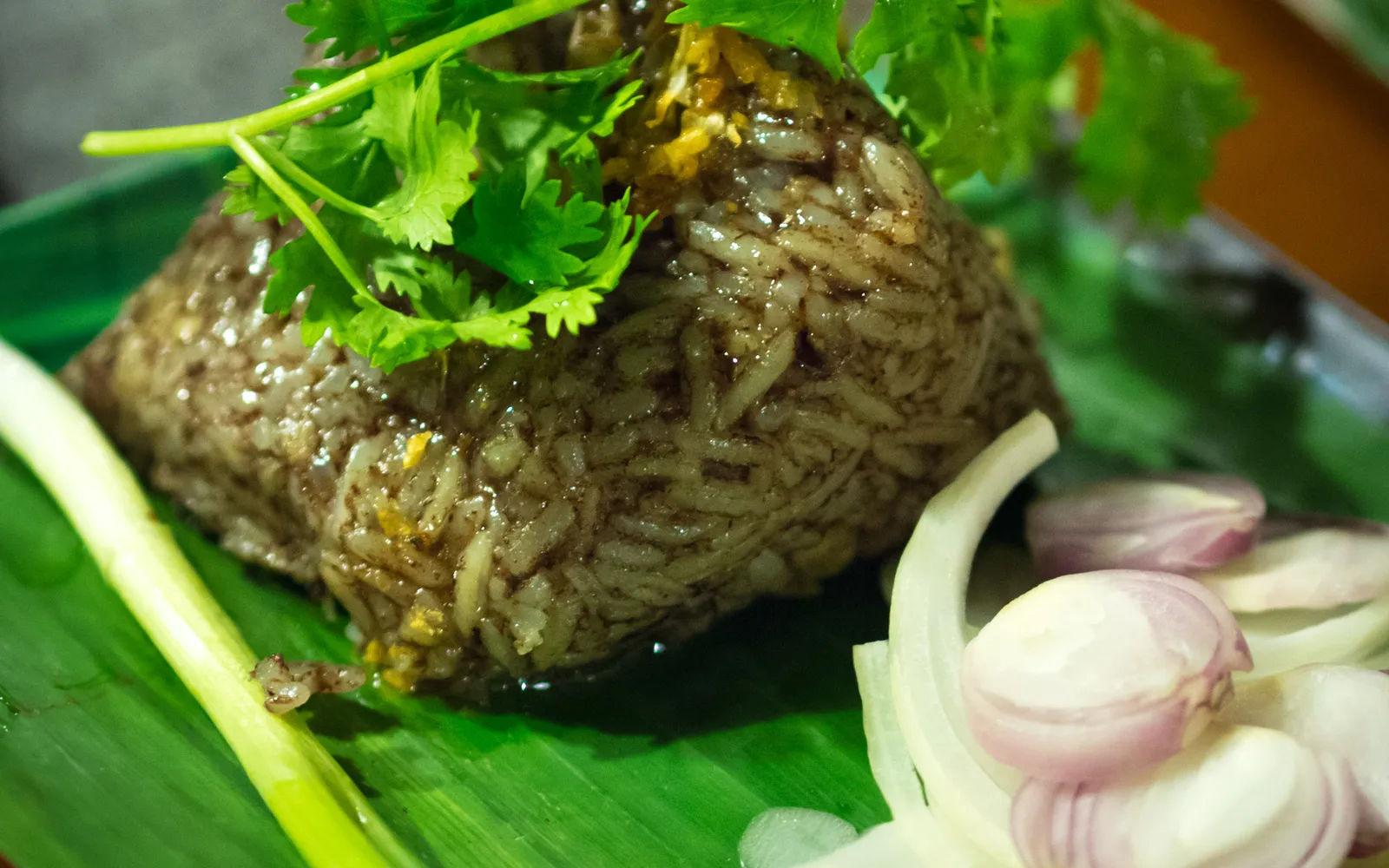 Khao kan chin wrapped in banana leaf — a deep red-brown sticky rice cake made with pork blood and minced pork, served on fresh banana leaf