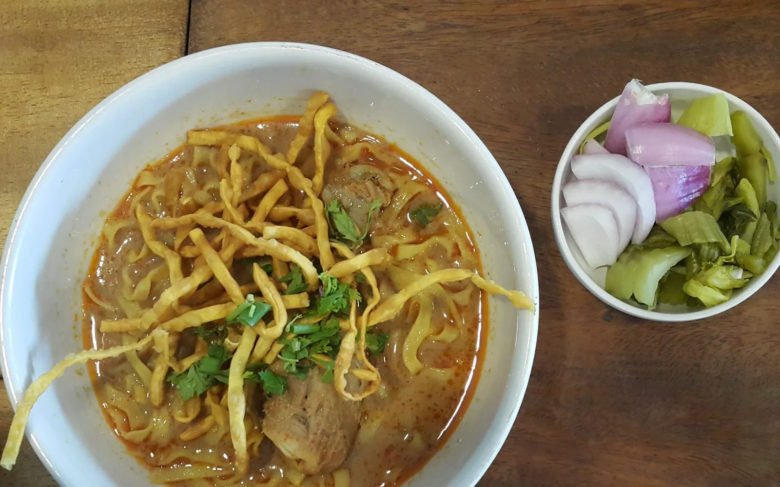 Chiang Rai khao soi: golden coconut curry broth with soft egg noodles, crispy fried noodles on top, shallots, pickled mustard greens, and lime on the side