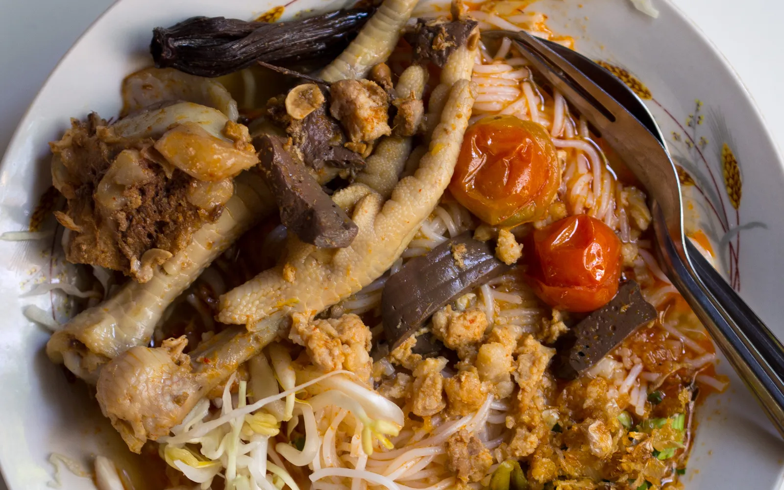 Lanna khanom chin nam ngiao — white rice vermicelli in a deep red-orange broth made from dried cotton tree flowers, with minced pork, fermented soybeans, and tomato