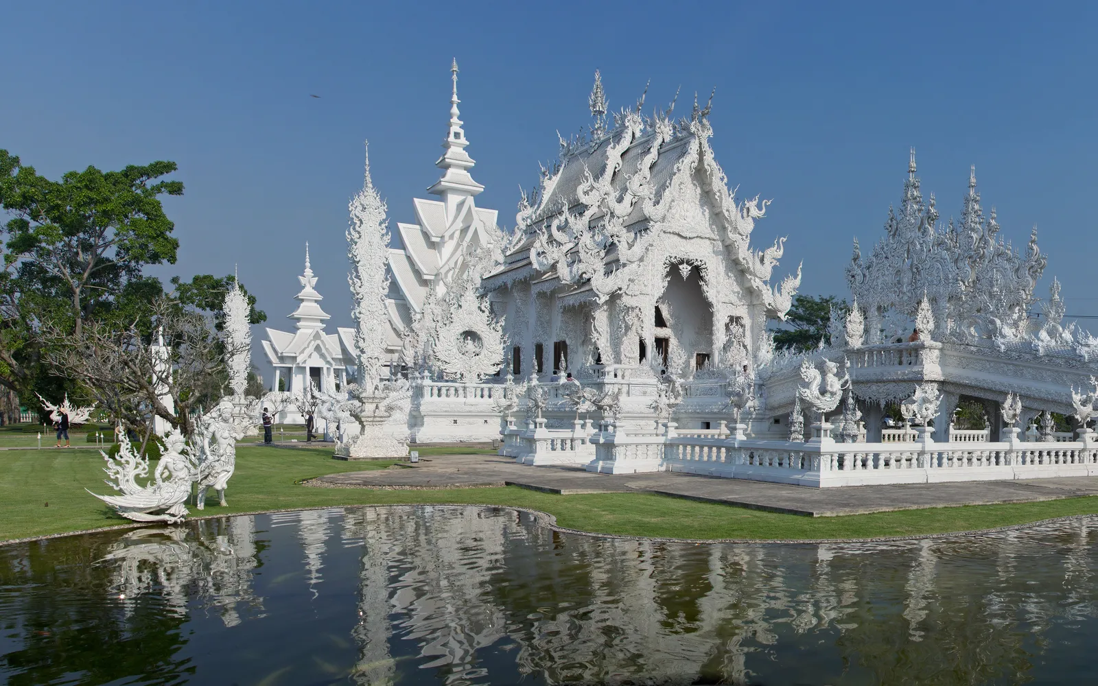 Wat Rong Khun in Chiang Rai — the white mirror-encrusted ubosot and bridge glittering in sunlight above a clear reflecting pool