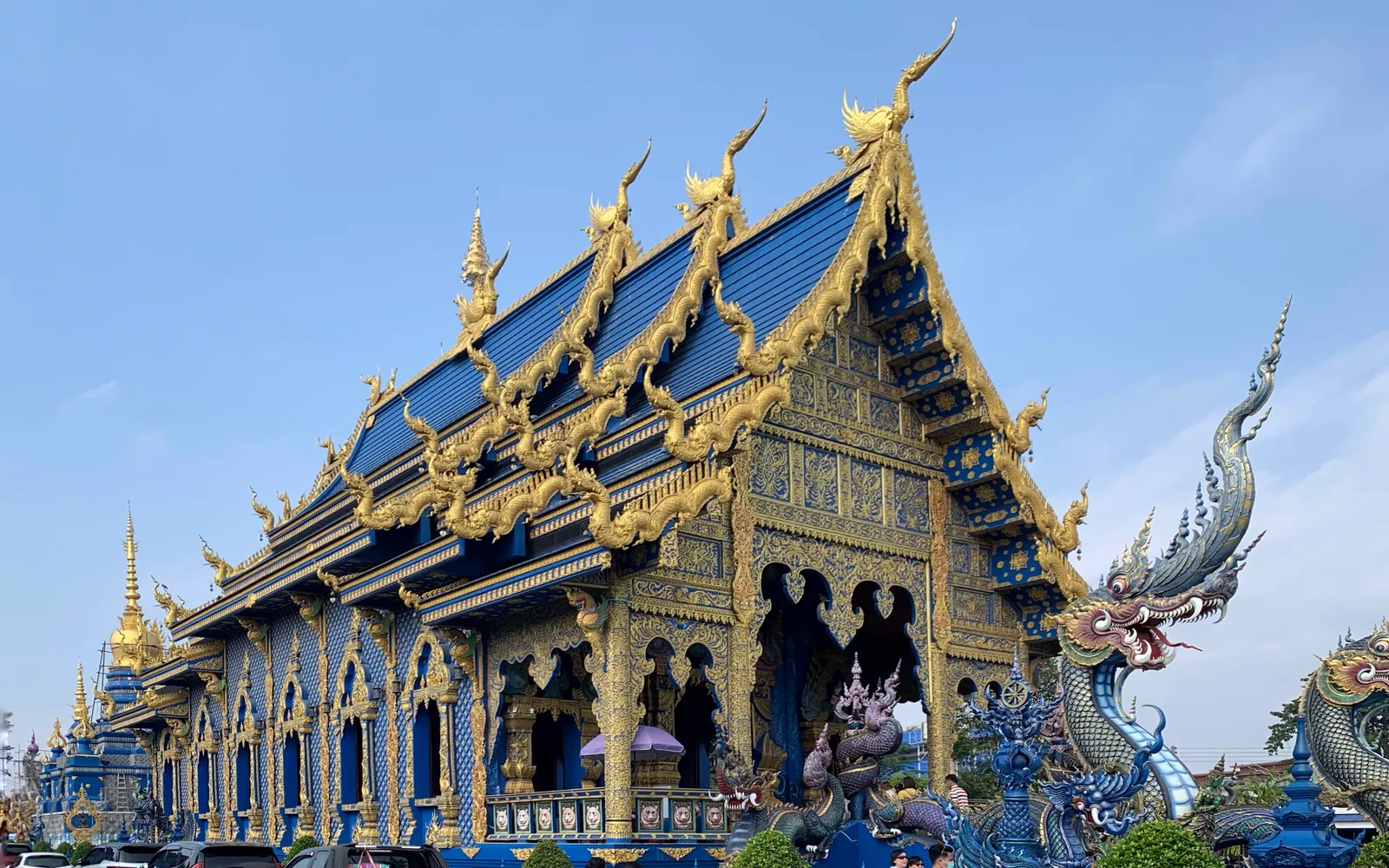 Wat Rong Suea Ten at night — the deep-blue viharn trimmed in gold blazes under floodlights, a white Buddha statue rising at the centre