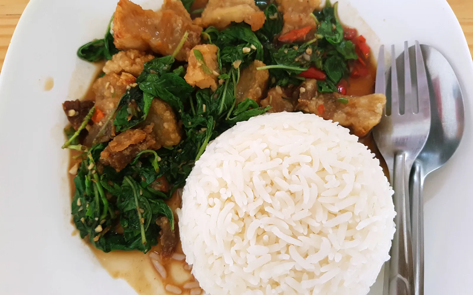 Stir-fried fresh prawn with Thai basil on steamed rice — bright green basil leaves, a golden fried egg, glossy oil over white rice