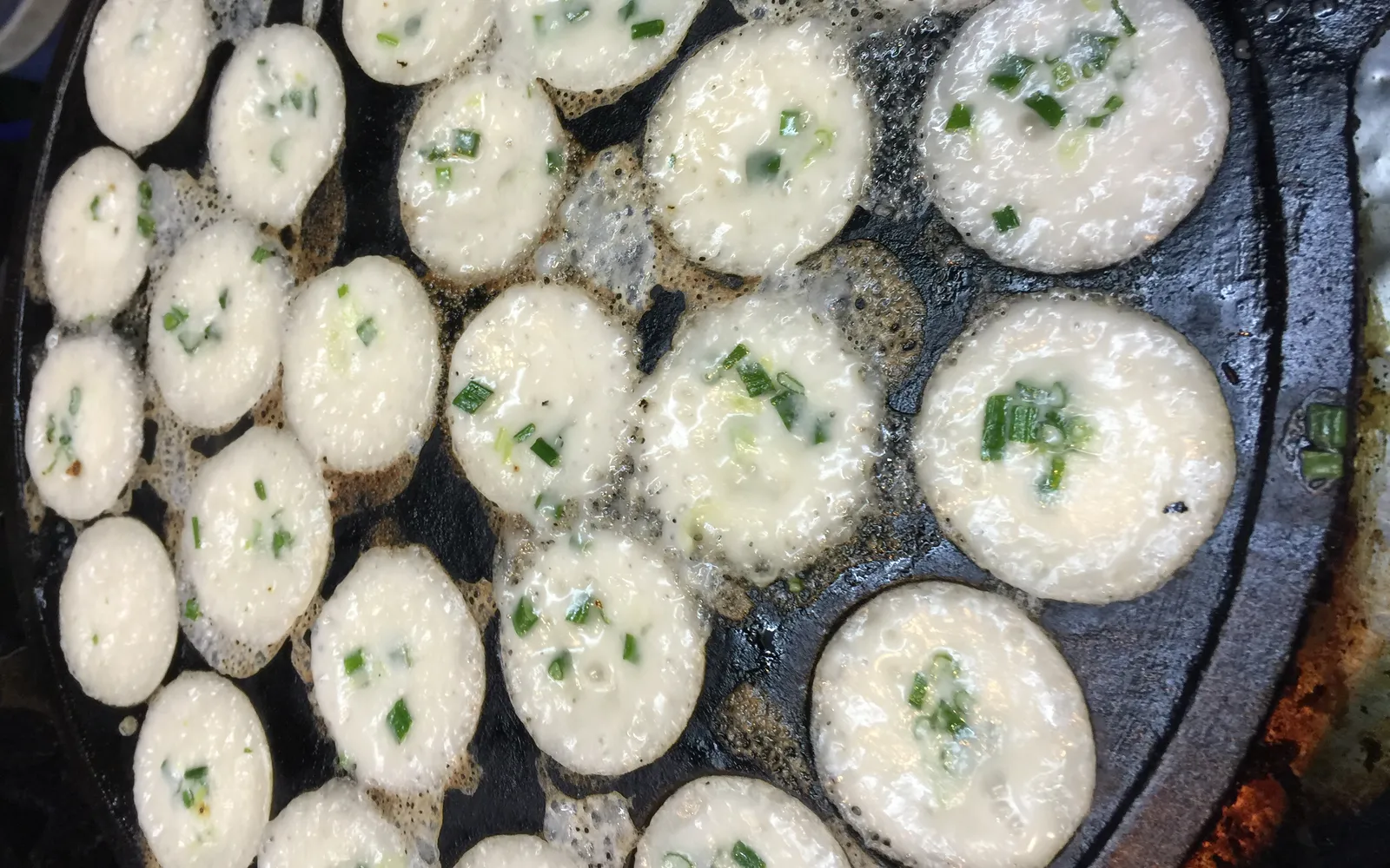 Khanom krok — coconut-milk rice-flour cakes in a round clay mould, pale white with golden edges, fragrant steam rising