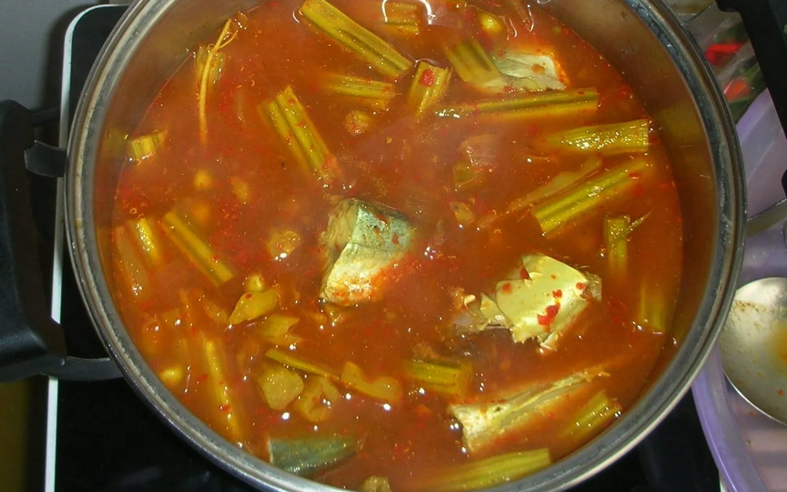 Southern kaeng som with fish and cha-om egg in a clay pot — deep orange-yellow broth fragrant with turmeric and Southern chillies