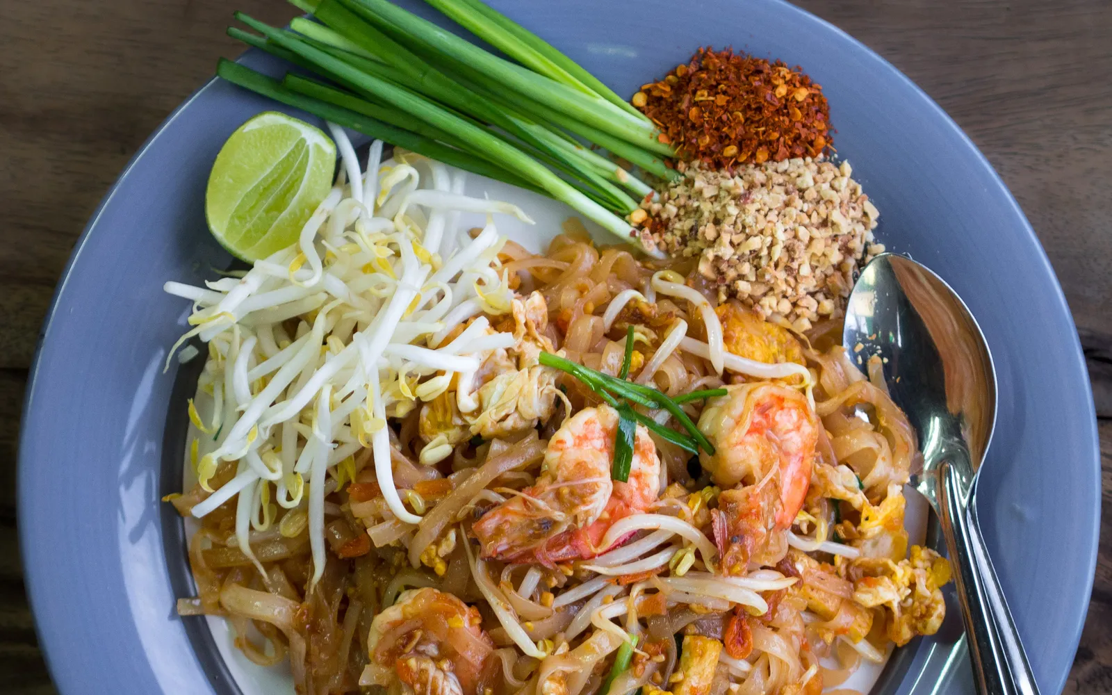 Pad thai with fresh shrimp in a cast-iron wok — rice noodles stir-fried with egg, bean sprouts, spring onions, and fresh prawns, topped with crushed peanuts, lime, and chilli flakes
